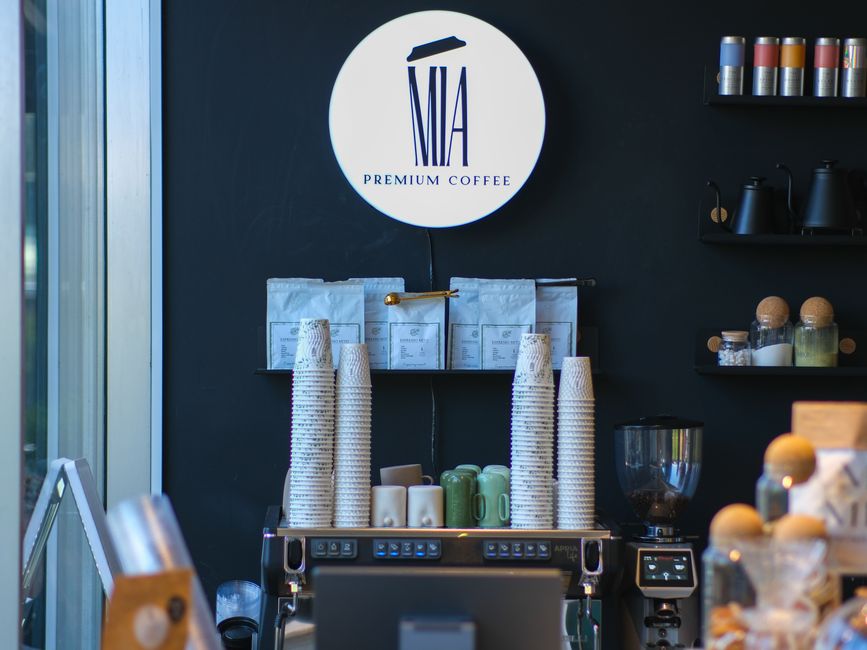 Cultura do Café — A stylish coffee shop interior featuring premium coffee branding, stacks of cups, and coffee brewing