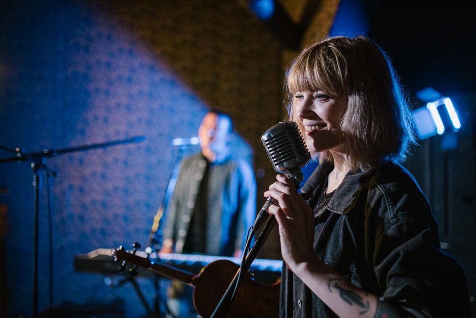Cultura do Café — Smiling caucasian woman singing with vintage microphone during live music performance.